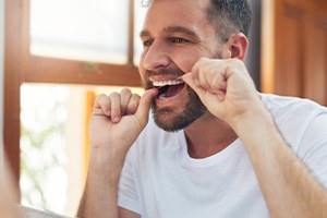 Man smiling while flossing in bathroom