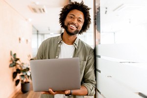 Man smiling while holding laptop in office