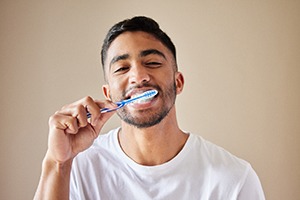 Man in white shirt smiling while brushing teeth