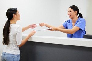 Dental receptionist smiling at patient while handing them forms 