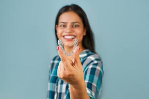 Woman smiling while holding up Invisalign aligner 
