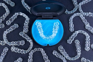 Bird’s eye view of many Invisalign trays surrounding carrying case on black surface