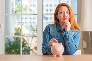 Woman putting coin in piggy bank for cost of veneers in Gainesville