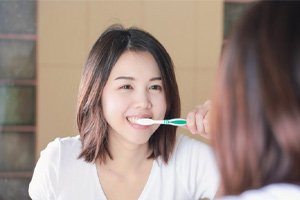 : woman brushing her teeth in front of mirror